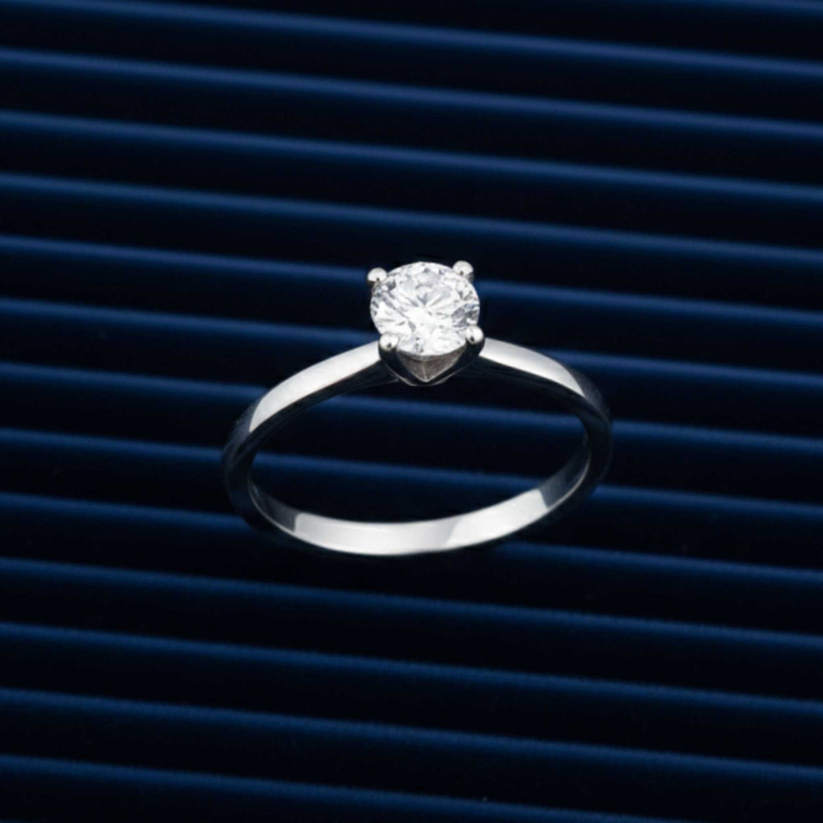 Anello solitario Artmid in oro bianco 18kt con diamante lab-grown 0.50 ct, disteso su velluto blu radiale.