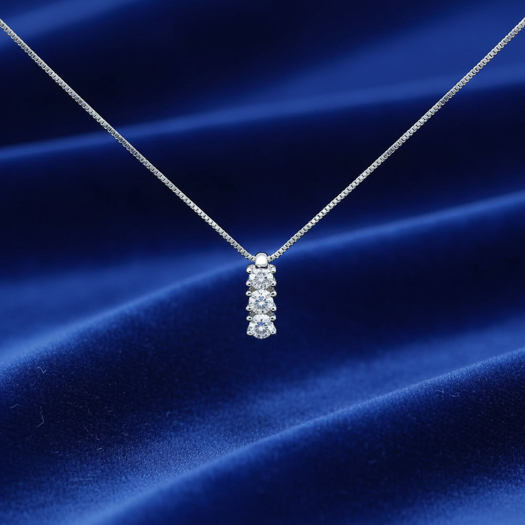 Collana Trilogy Art MiD in oro bianco 18kt con tre diamanti naturali da 0.12 carati su sfondo velluto blu ondoso.