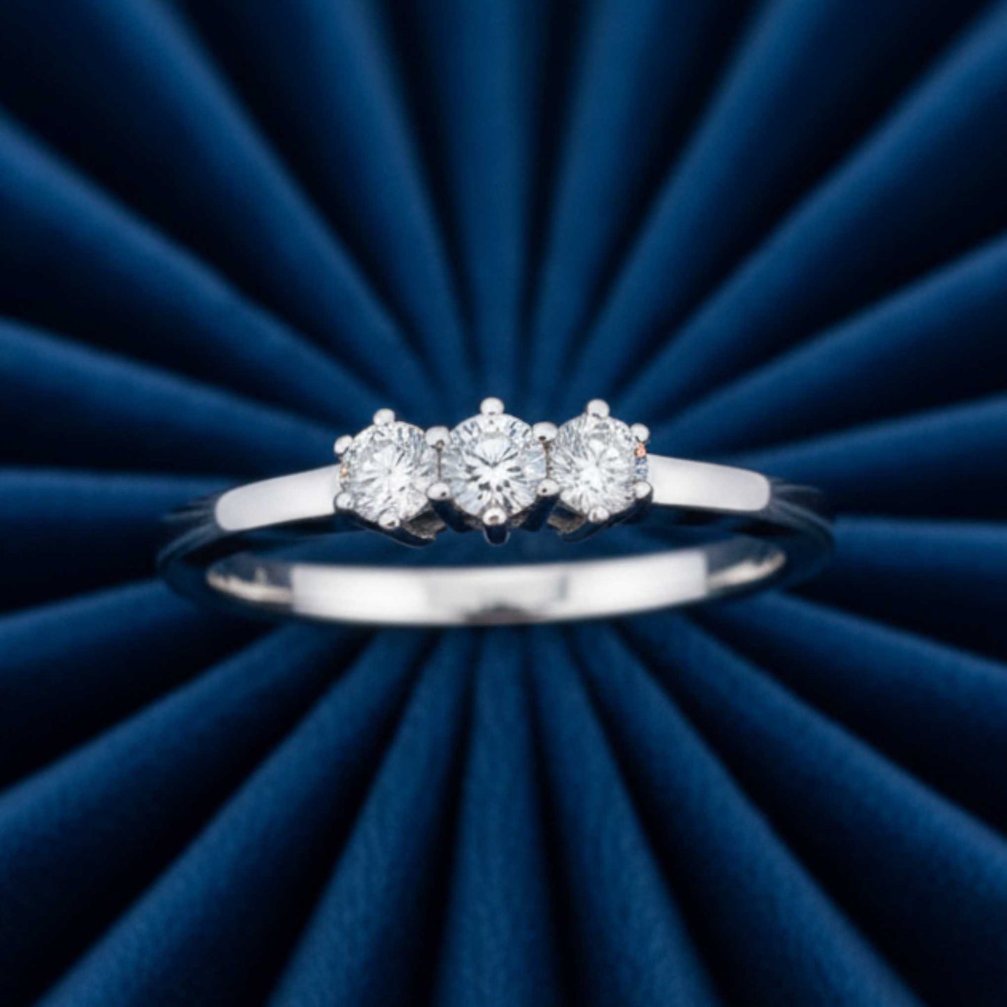 Anello Trilogy ArtMID in oro bianco 18kt con tre diamanti naturali adagiato su velluto burgundy radiale.