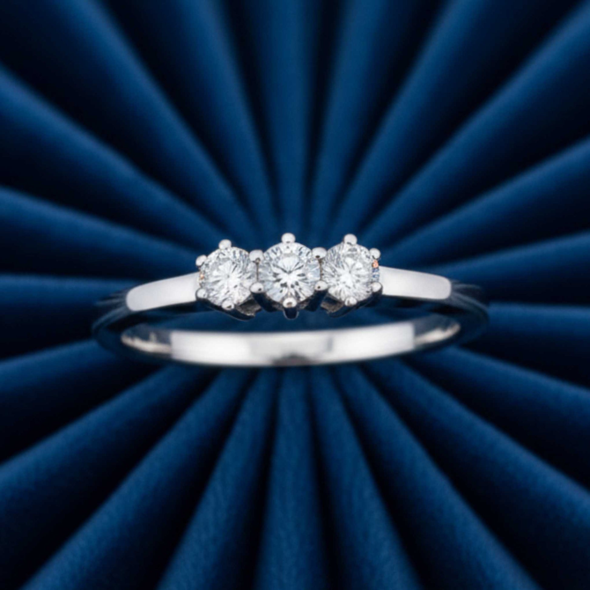 Anello Trilogy ArtMID in oro bianco 18kt con tre diamanti naturali adagiato su velluto burgundy radiale.